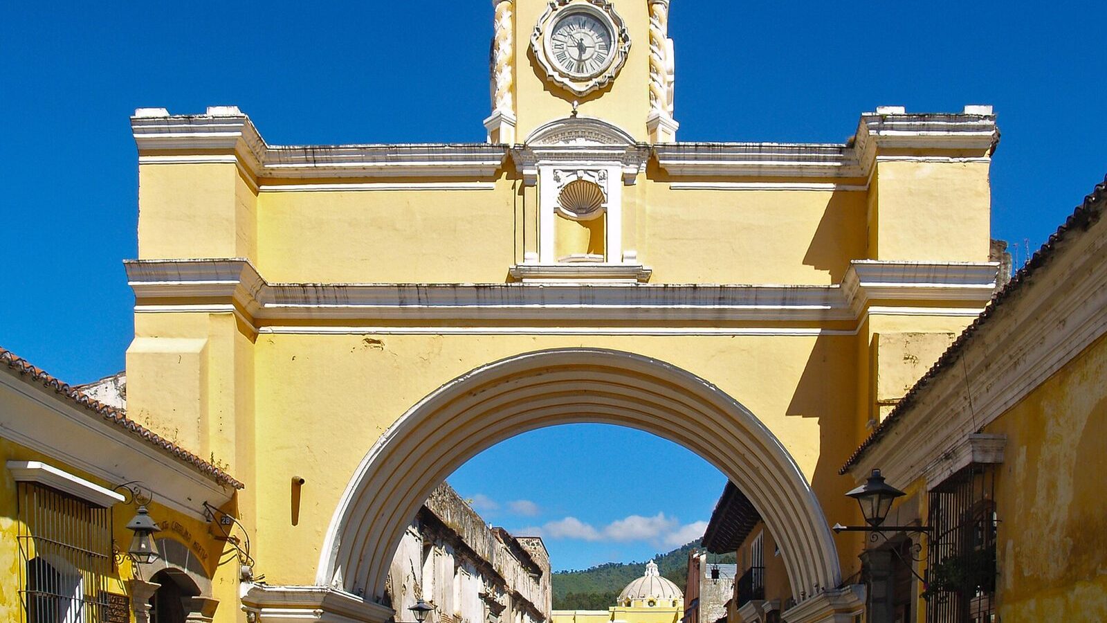 Arco de Santa Catalina de Antigua Guatemala, de fachada amarilla, con el reloj y la calle empedrada al fondo