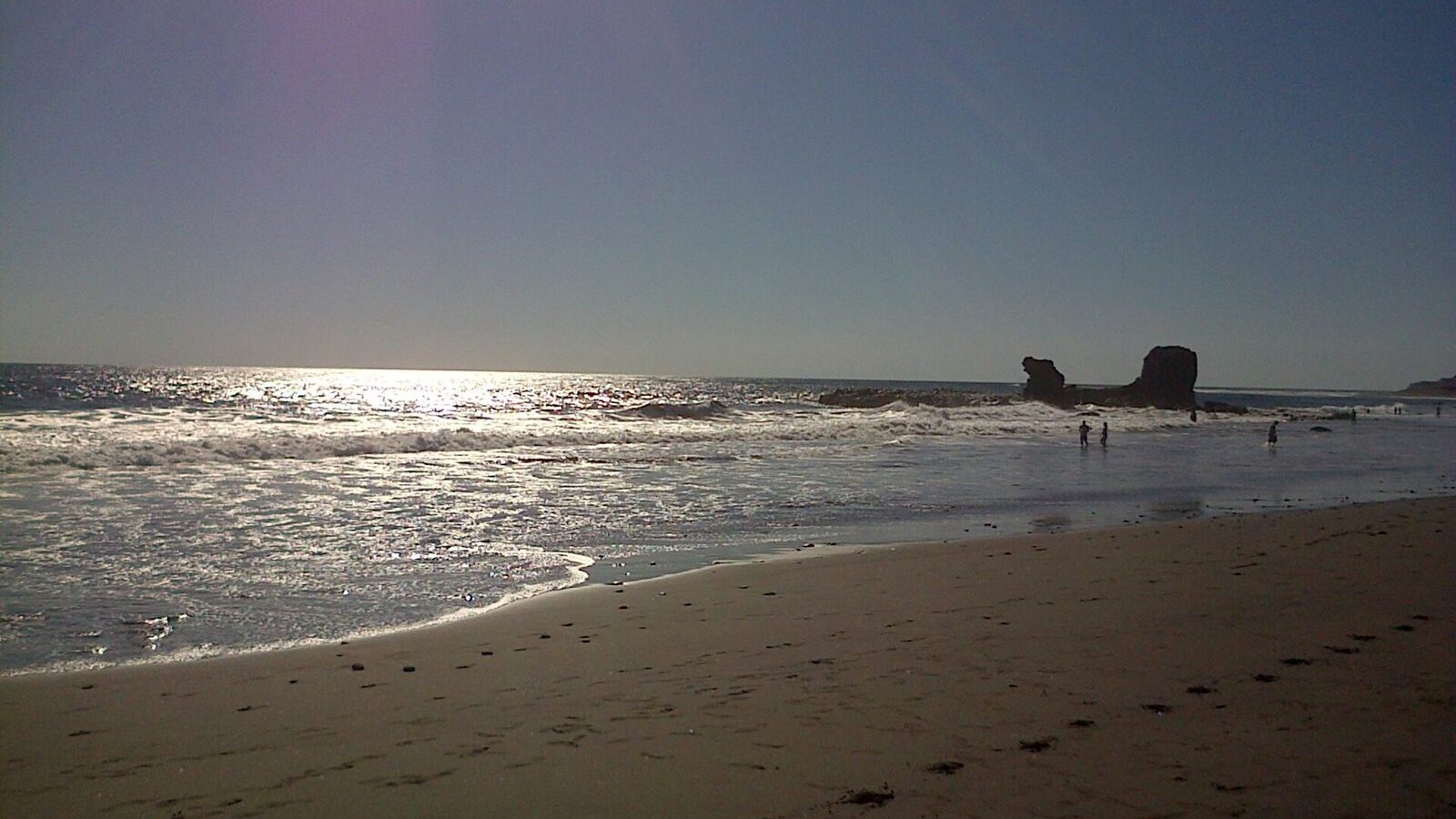 Playa salvadoreña del Pacífico al atardecer con el sol reflejado sobre la arena mojada