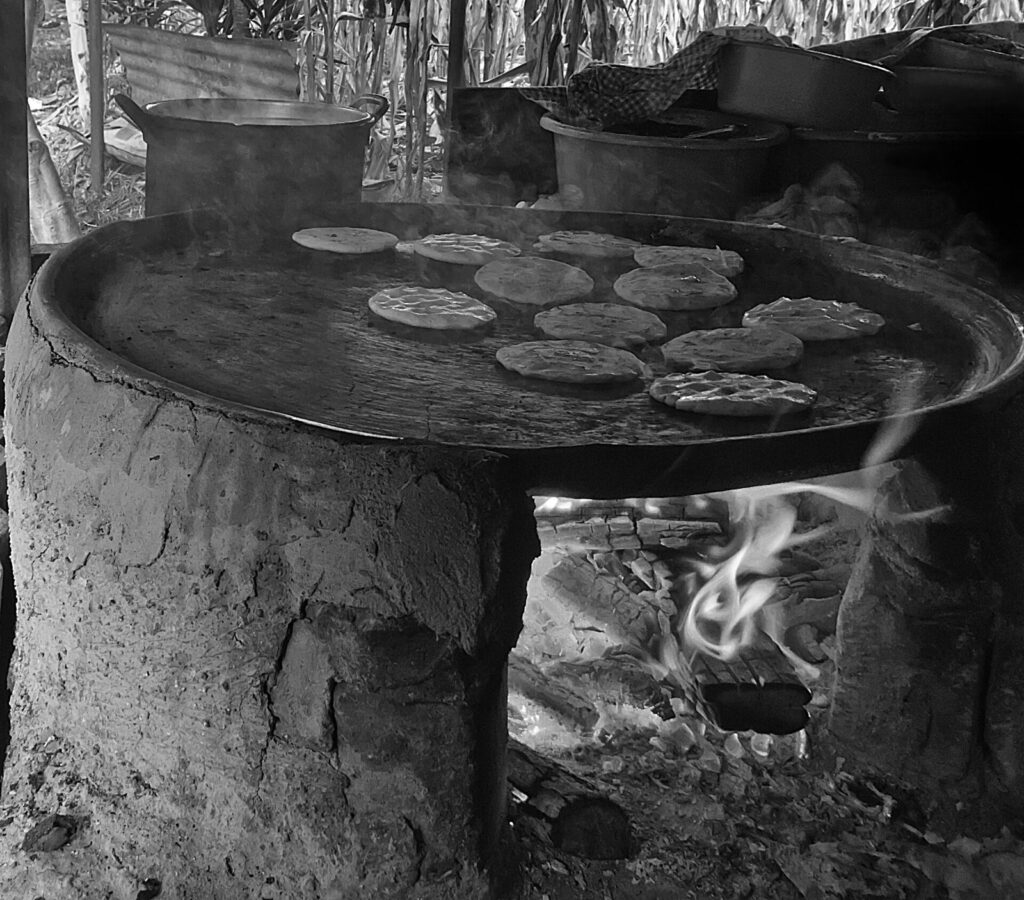 Pupusas cociéndose sobre un comal de barro a fuego de leña