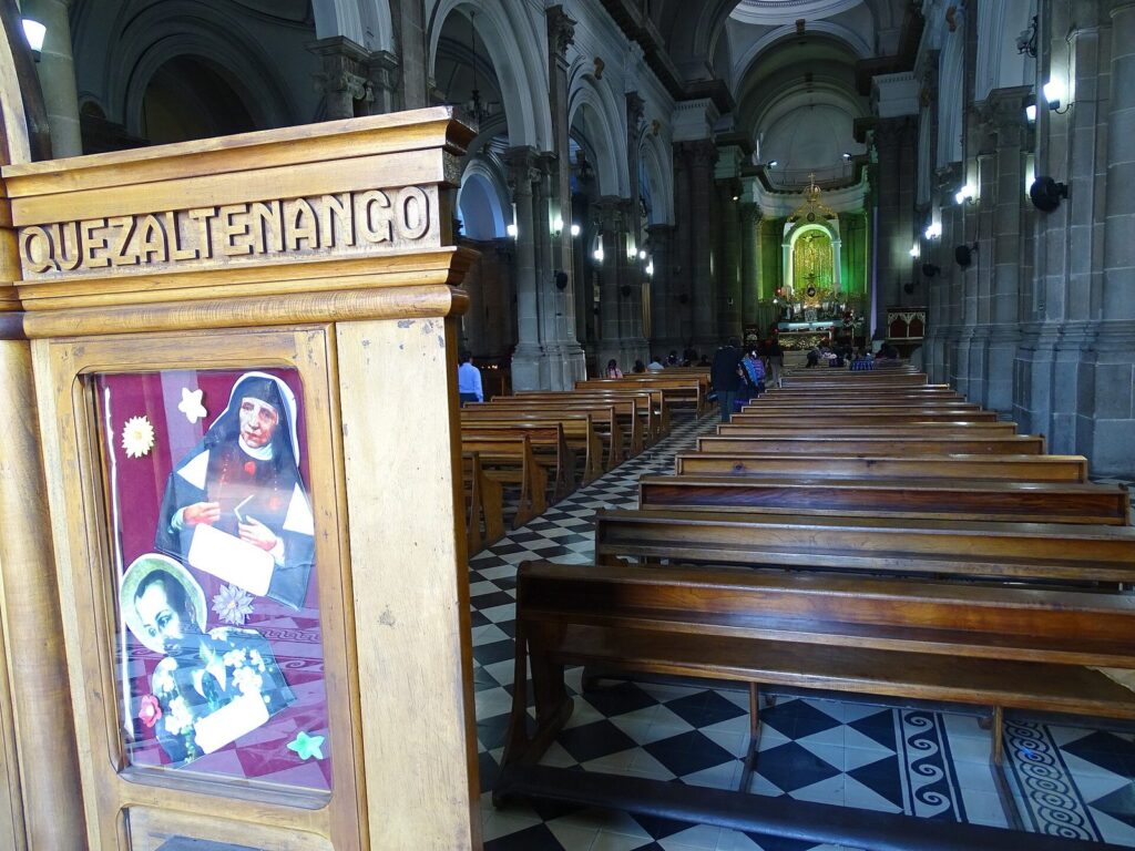 Interior de la catedral de Quetzaltenango con bancos de madera y suelo ajedrezado