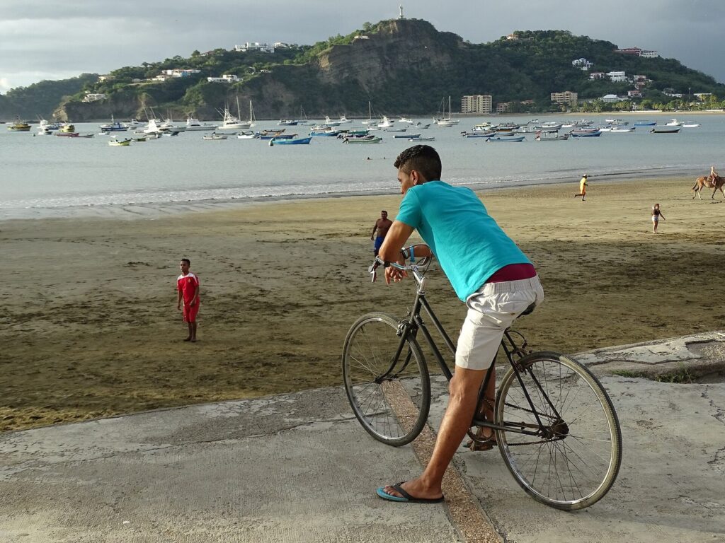 Ciclista en la playa de San Juan del Sur con la bahía y las colinas al fondo