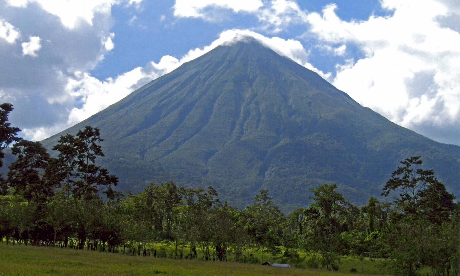 Cono perfecto del volcán Arenal en Costa Rica sobre praderas verdes