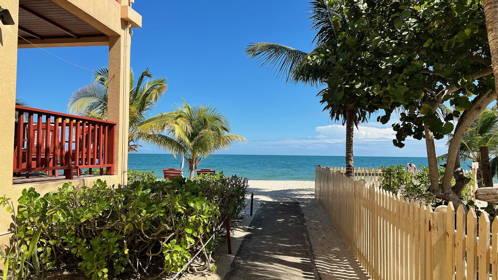 Acceso a la playa entre casas de madera en Placencia, Belice, con palmeras y el mar al fondo
