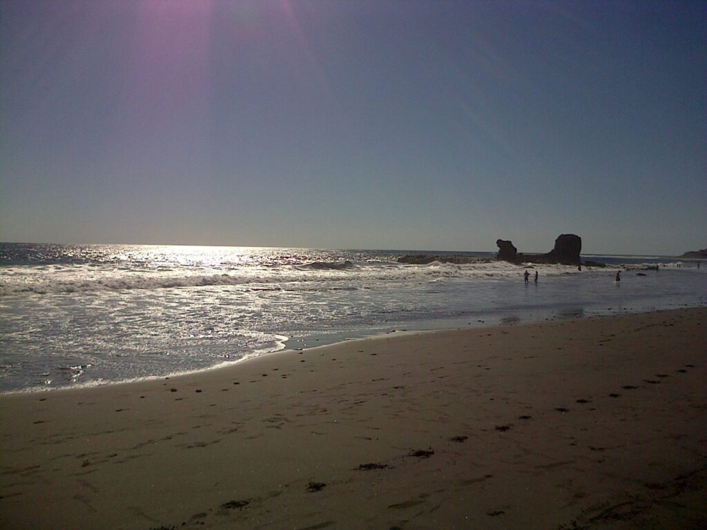 Playa de arena oscura de El Tunco con el sol reflejado en el agua