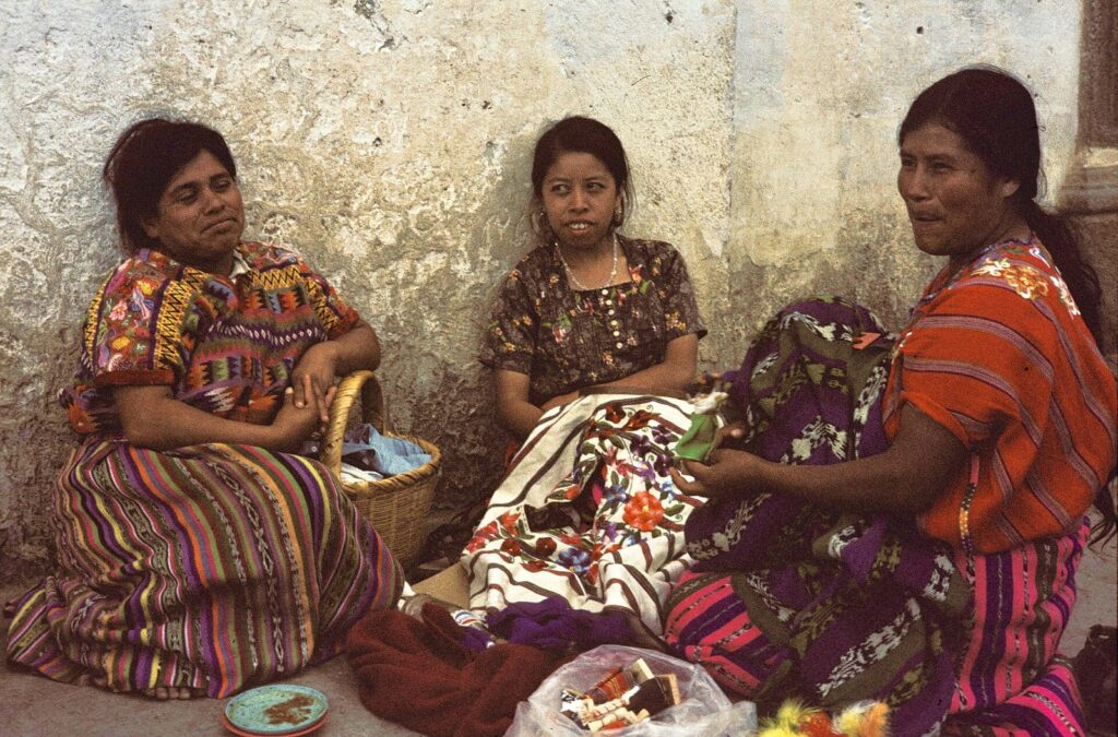 Tres mujeres mayas con huipiles tradicionales tejiendo en el altiplano de Guatemala